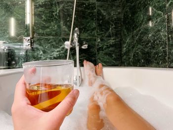 Cropped hand of woman holding drink while relaxing in the bathtub 