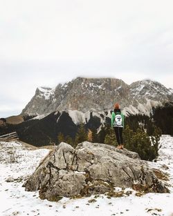 Rear view of woman standing on rock against mountains during winter