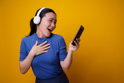 Young woman using mobile phone against yellow background