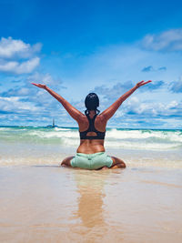 Young woman with arms raised on beach against sky