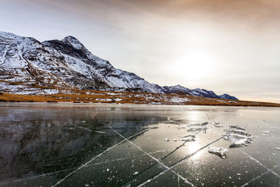 Scenic view of frozen lake by snowcapped mountain against sky