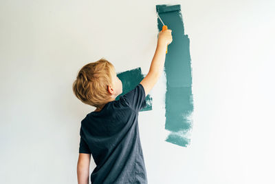 Rear view of boy painting wall at home