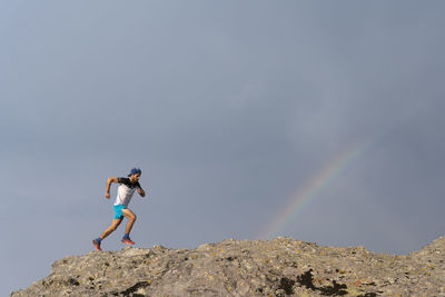 One man trail running on a rocky terrain with a rainbow