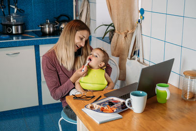 Work from home. young mother with baby girl working at home using laptop on kitchen background 