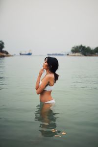 Young woman wearing bikini standing in sea against clear sky