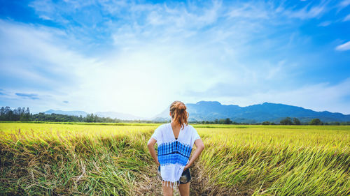 Rear view of woman standing on field against sky