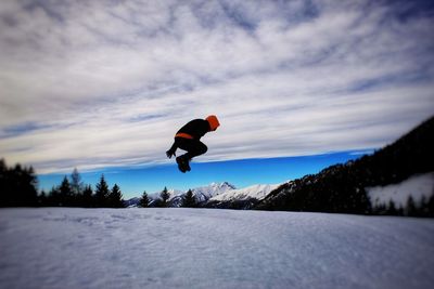 Man jumping on snowcapped mountain against sky