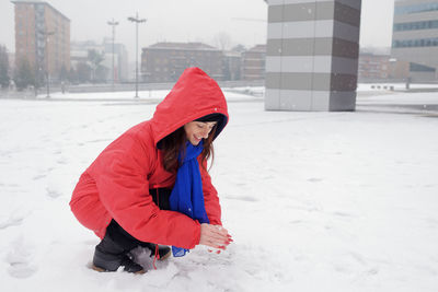 Full length of woman crouching on snow covered outdoors