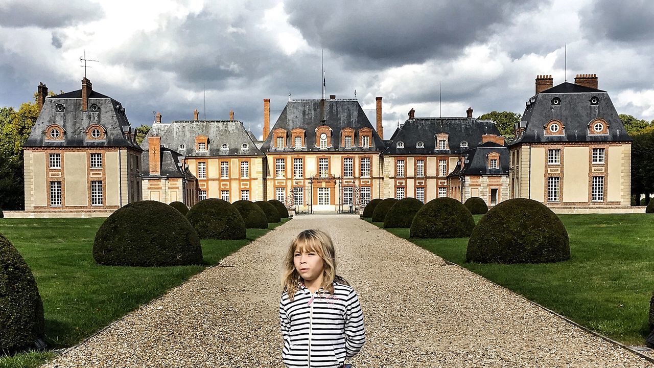 WOMAN IN FRONT OF GARDEN BY LAWN AGAINST CLOUDY SKY