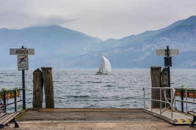 Sailboat at lake by mountain against cloudy sky