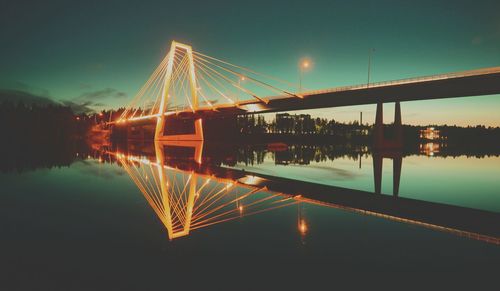 Illuminated bridge over river against sky at night