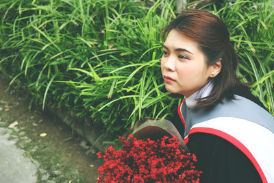 Young woman wearing graduation gown with bouquet