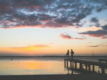 Silhouette people on beach against sky during sunset