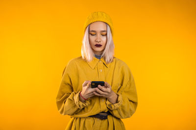 Young man using mobile phone against yellow background