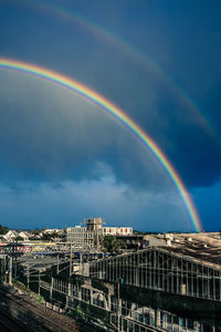 Rainbow over industrial buildings by rail tracks in city against gloomy sky