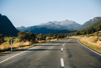 Road leading towards mountains against clear sky