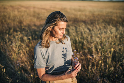 Blond woman looking at flowers at field during weekend