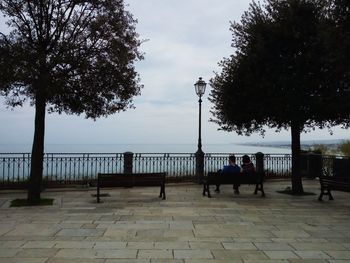 People on sidewalk by sea against sky