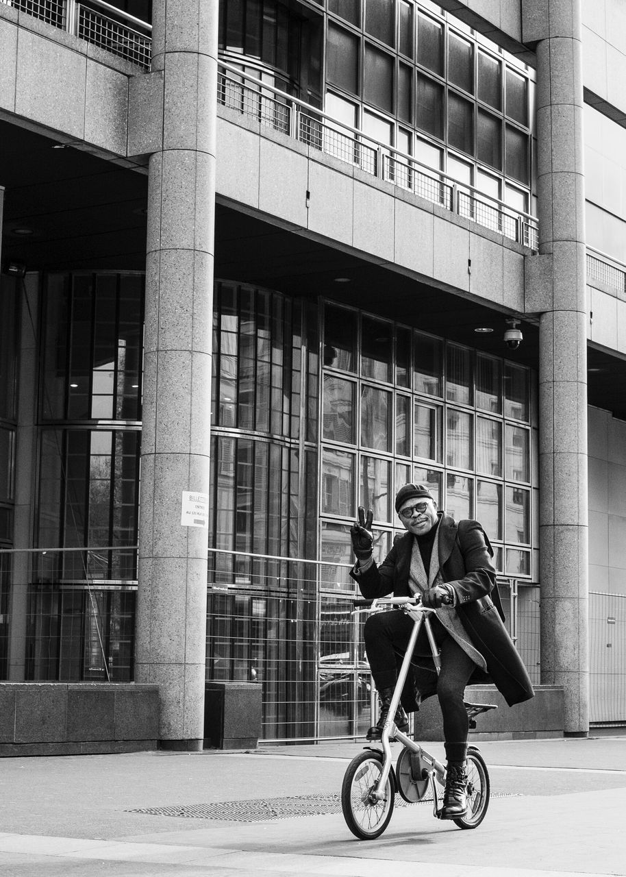 building exterior, architecture, bicycle, built structure, land vehicle, transportation, mode of transport, full length, lifestyles, men, riding, city, leisure activity, building, side view, street, window, day
