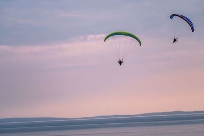 People paragliding over sea against sky during sunset