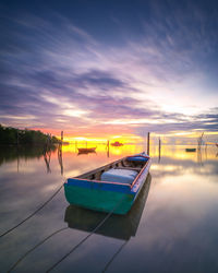 Boat moored in lake against sky during sunset