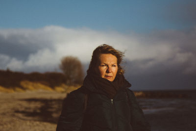 Mature woman wearing warm clothing looking away while standing against cloudy sky