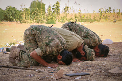 Men praying while sitting on land against trees