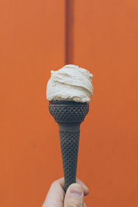 Human hand holding ice cream on a orange colored background