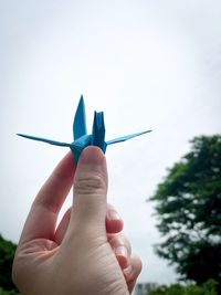 Close-up of hand holding paper crane against sky