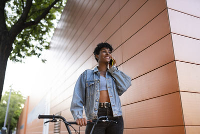 Young woman with bicycle standing against wall