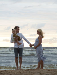 Man with daughter holding pregnant woman hand at beach