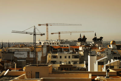 Cranes amidst buildings in city against clear sky