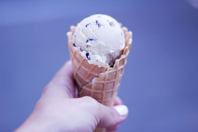 Close-up of hand holding ice cream against blue sky