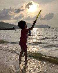 Full length of boy holding toy on shore at beach during sunset