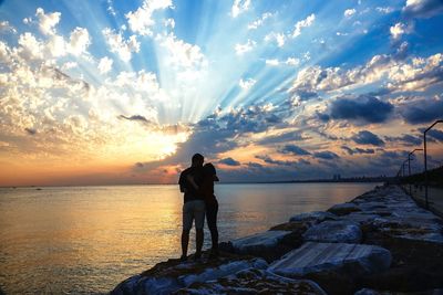 Rear view of man standing on rock against sea during sunset