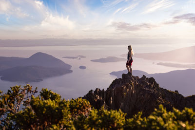 Man standing on rock looking at mountains against sky