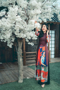 Smiling young woman standing by tree