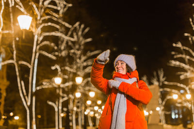 Woman standing by illuminated tree at night during winter