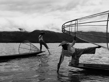 Men fishing in sea while traveling on boat against cloudy sky