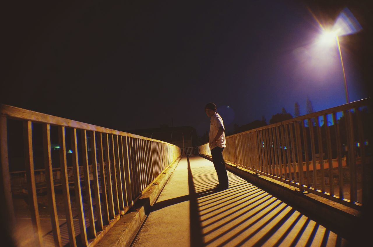 full length, lifestyles, leisure activity, walking, railing, men, rear view, night, the way forward, built structure, person, transportation, bicycle, illuminated, architecture, bridge - man made structure, casual clothing, silhouette