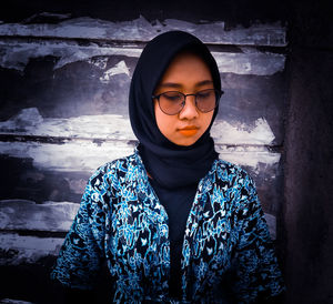 Portrait of young woman looking away while standing against wall