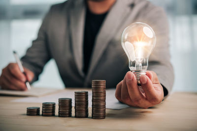 Midsection of man holding illuminated light bulb