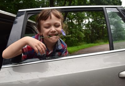 Portrait of a happy boy with flower in his mouth looking through the car window