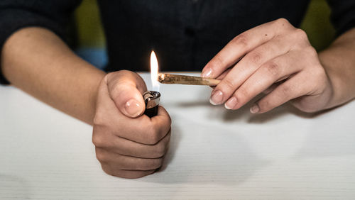 Midsection of woman burning marijuana joint on table