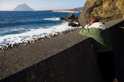 Rear view of woman leaning on retaining wall by sea