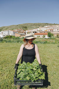 Happy farm worker with crate of leafy vegetables standing at field