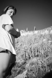 Low angle portrait of young woman standing on grassy field against sky