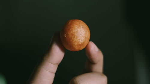 Close-up of hand holding apple against black background