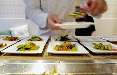 Midsection of chef serving food on plates in kitchen