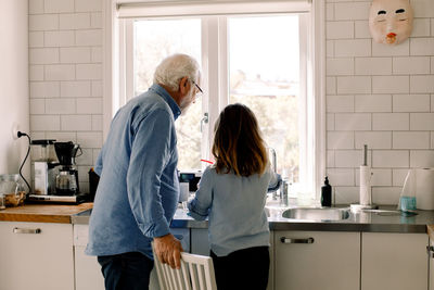 Grandfather and granddaughter standing at counter in kitchen